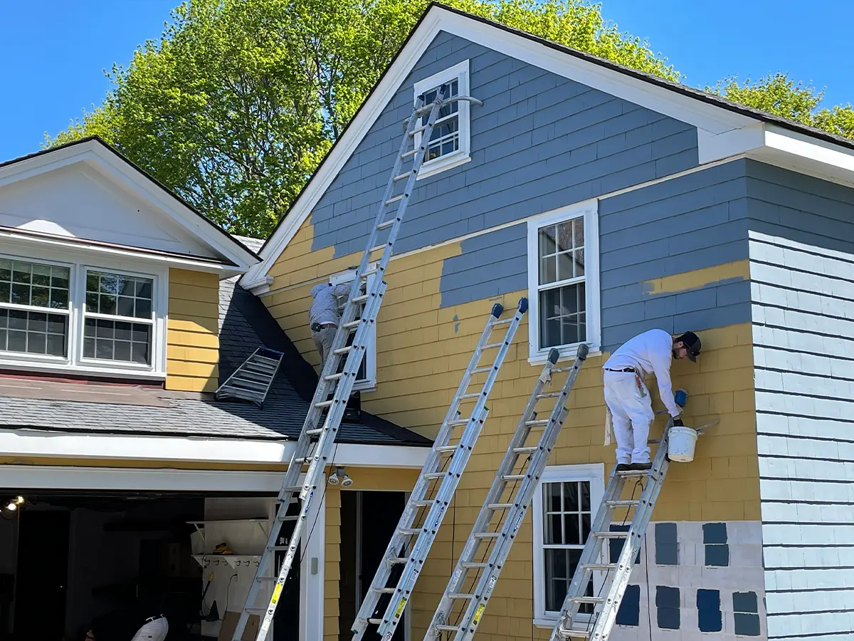 Experienced painter using ladder and sprayer for high-quality finish on Concord, NC home’s exterior siding